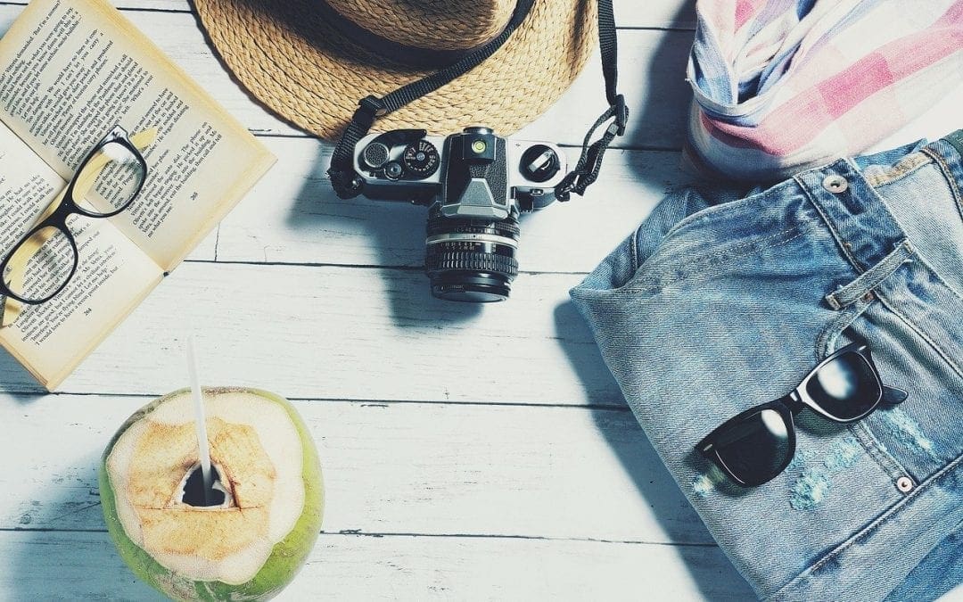 a book, camera, sunglasses, and coconut drink arranged on a table