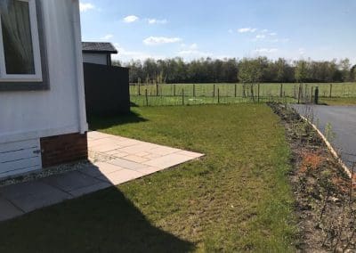 Backyard of a house with a brick patio and a grassy field beyond the patio.