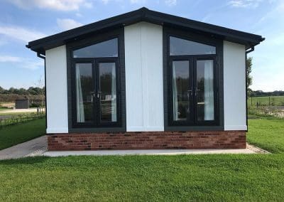 Small house with a brick foundation, two windows, and a metal roof in a grassy field in Omar Newmarket.